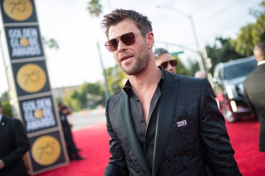 Chris Hemsworth wore his “Times Up “ badge in a black suit showing off his chest with his top buttons undone and wearing sunglasses © HFPA