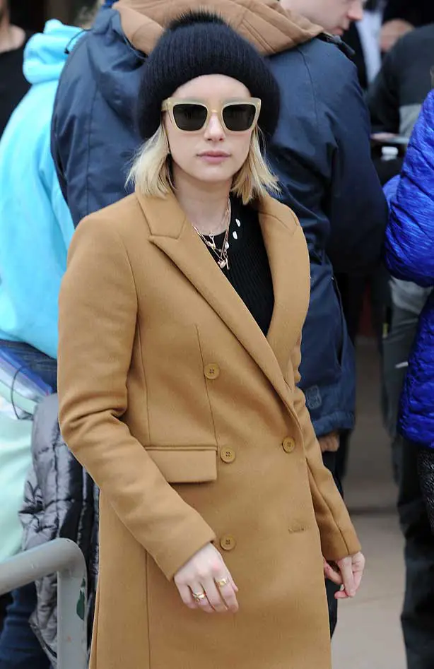 Emma Roberts in tan winter jacket with a black winter bobble hat and oversized sunglasses